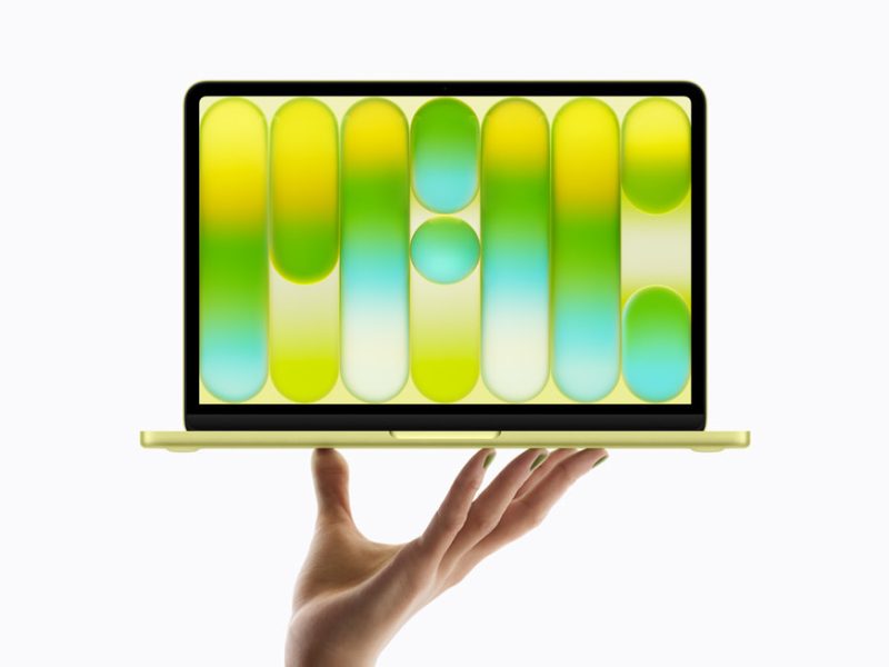 Citrus színű MacBook Neo nyitott kijelzővel, egy kéz felett.