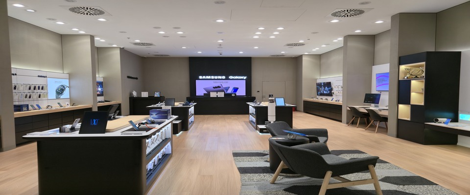 Samsung Experience Store belső tere demóasztalokkal, kijelzőkkel és Galaxy felirattal.