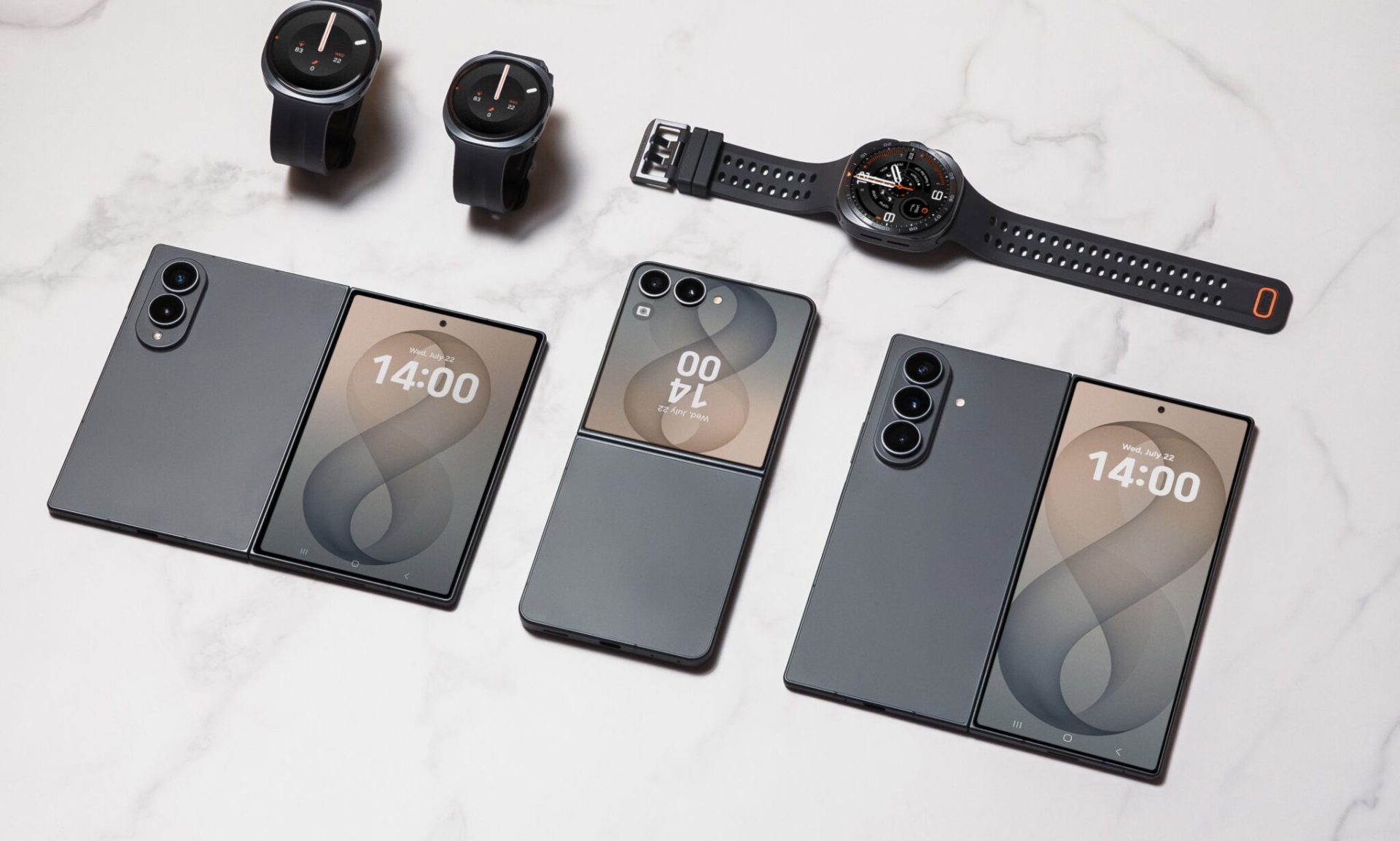 Samsung Galaxy hajlítható telefonok és Galaxy okosórák fehér felületen elrendezve.