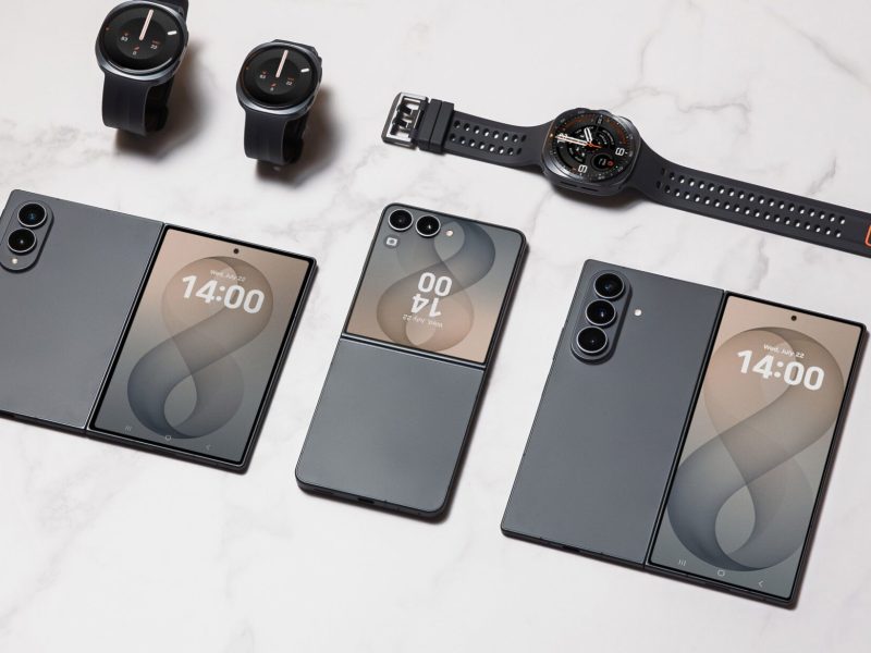 Samsung Galaxy hajlítható telefonok és Galaxy okosórák fehér felületen elrendezve.