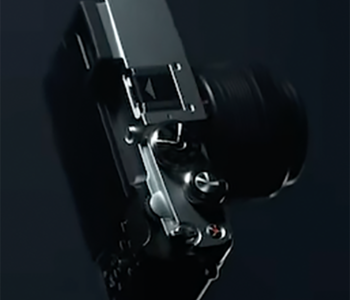 Sötét teaser-képkocka az OM System új, PEN-F ihletésű kamerájának felső részéről.