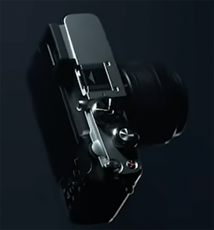 Sötét teaser-képkocka az OM System új, PEN-F ihletésű kamerájának felső részéről.