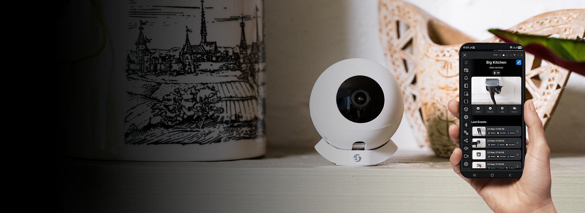 Fehér Shelly Camera egy polcon, mellette telefonon a Shelly Smart Control kameraeseményei.