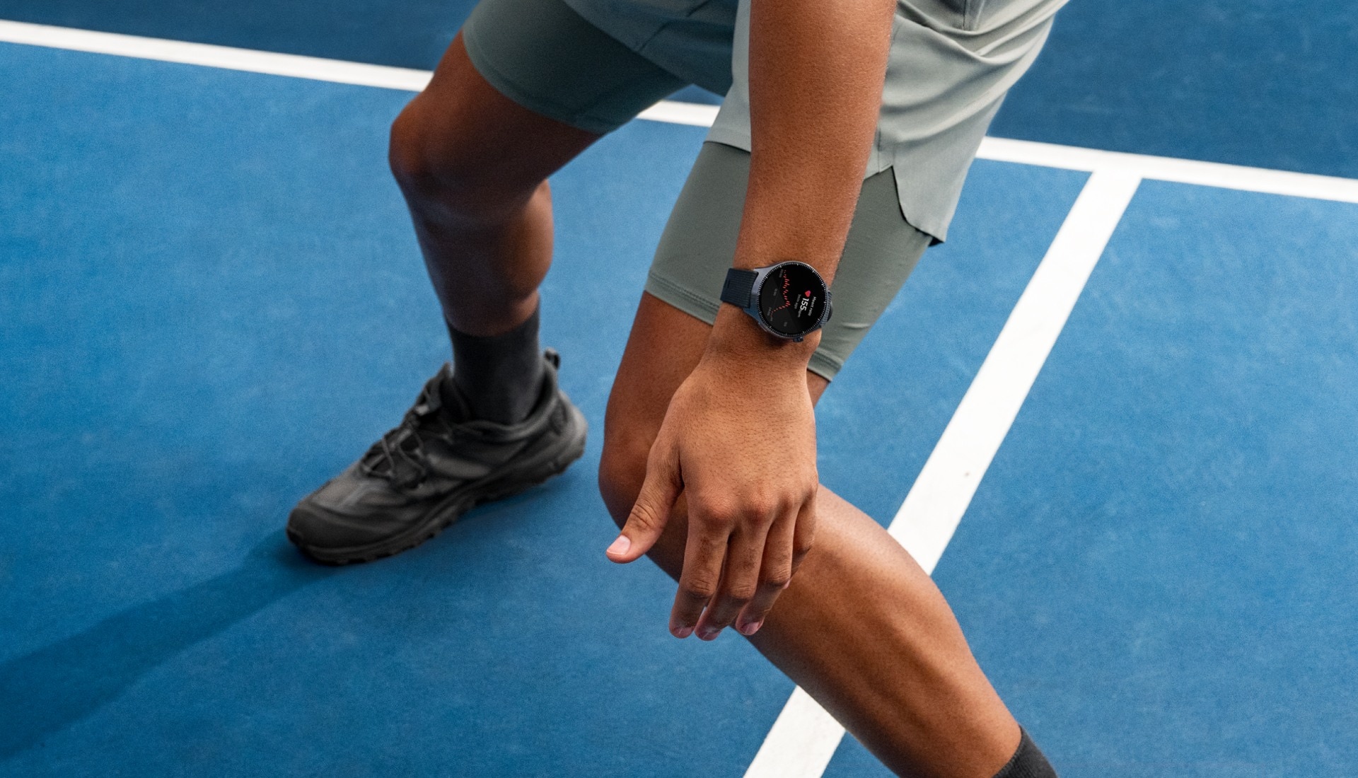 Sportoló rajtpozícióban egy kék pályán, csuklóján fekete Moto Watch Ultra okosórával.